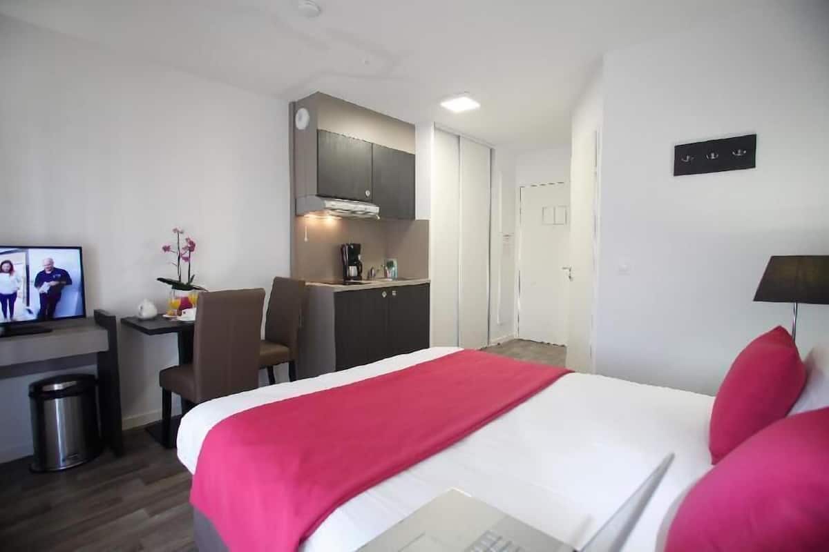 Una habitación de hotel con cama, escritorio, silla, una pequeña kitchenette y televisor.