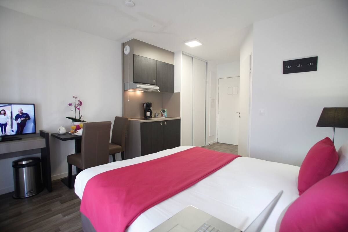 Een hotelkamer met een bed, een bureau met stoel, een kitchenette en een televisie.