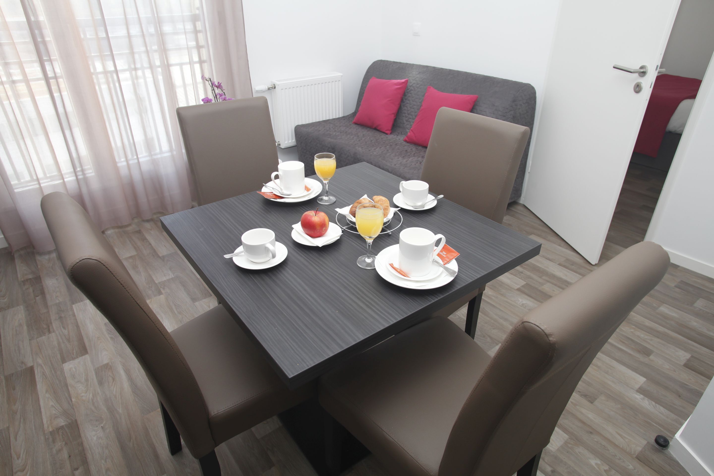 Comedor con una mesa lista para el desayuno, incluyendo platos, tazas y un vaso de jugo de naranja.