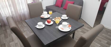 Comedor con una mesa lista para el desayuno, incluyendo platos, tazas y un vaso de jugo de naranja.