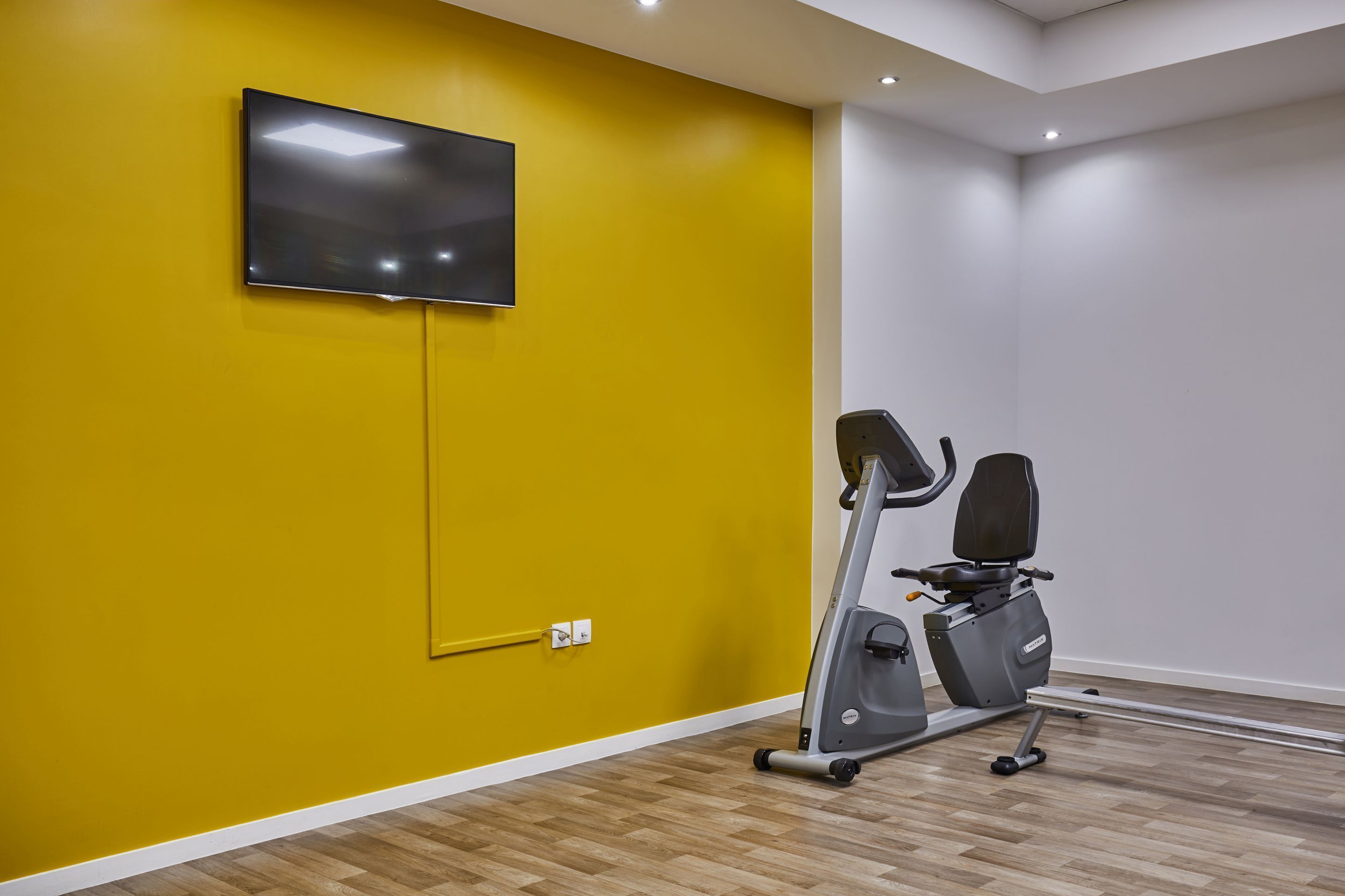 A room with a yellow wall, a mounted TV, and a stationary exercise bike.
