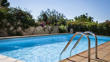 Relax by the pool surrounded by lush greenery and a deck.