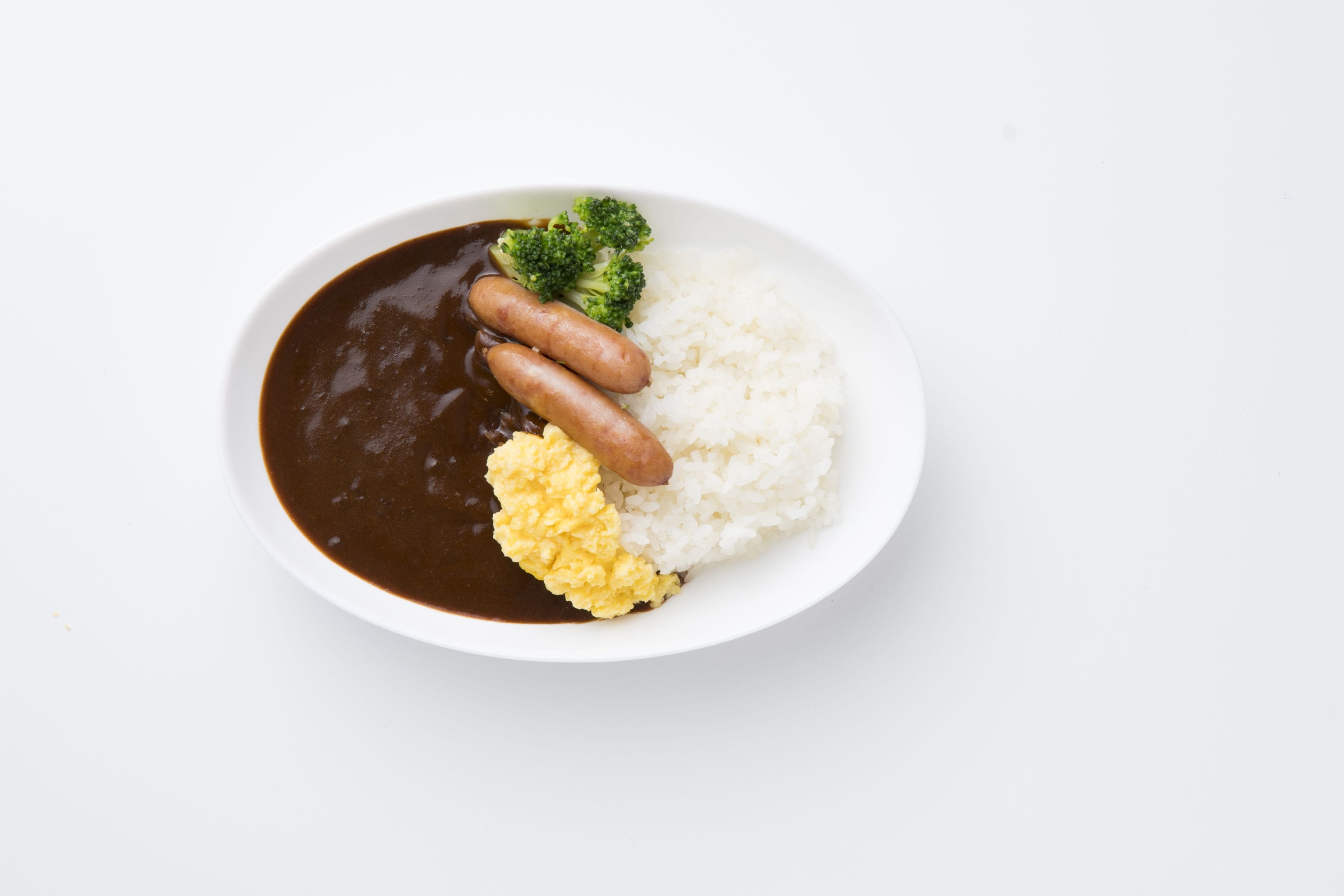 A white plate with white rice, two sausages, scrambled eggs, and broccoli.