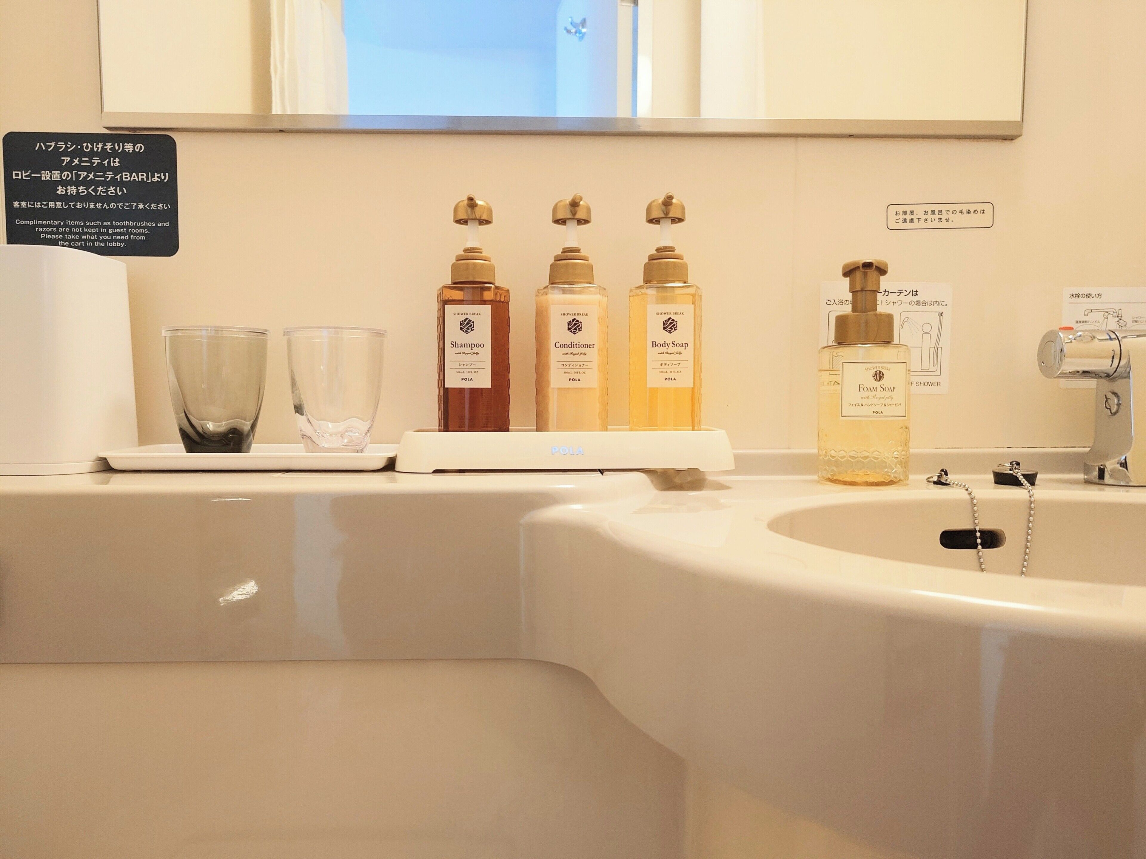 A bathroom with a sink, three toiletry bottles, a glass, and a sign with Japanese text.