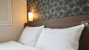 Habitación de hotel con cama, almohadas blancas, cabecera, lámpara de pared y pared con estampado geométrico.