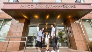 La entrada del Sanco Inn Kuwana-Ekimae, con vista clara del nombre del hotel y una familia posando frente a él.