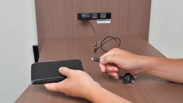 A person holding a black smartphone in a wooden room with a power outlet and cable on the wall.