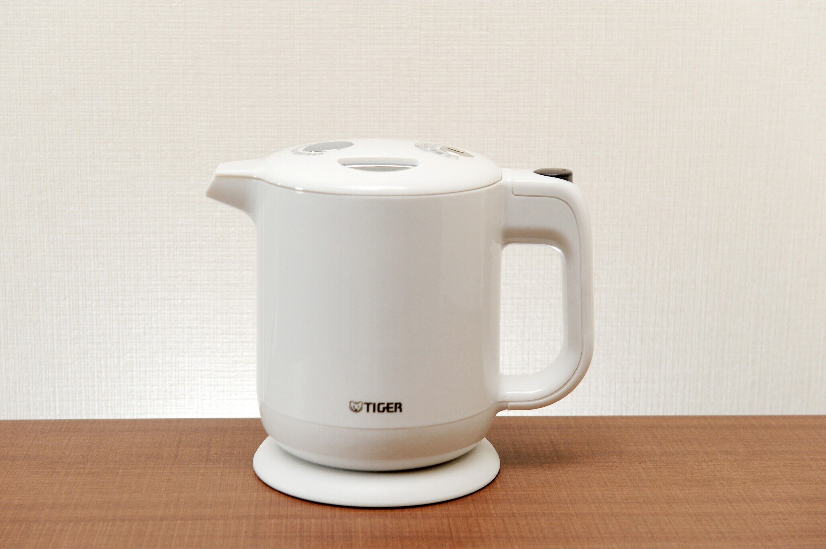 A white electric kettle with a handle and spout, placed on a wooden surface.
