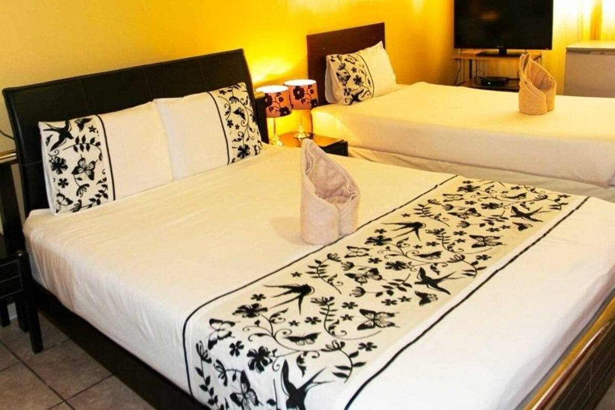 A hotel room with two beds, each with a floral bedspread and matching pillows. There is a television on a stand and a small table with a lamp and a towel.