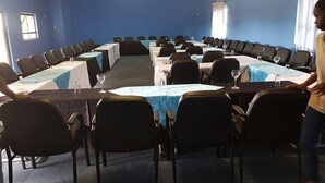 Un salón de conferencias con una larga mesa, sillas y una persona de pie junto a la mesa.
