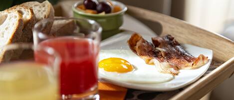 A breakfast tray with toast, a fried egg, bacon, a glass of red juice, and a bowl of fruit.