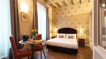 A hotel room with a bed, a dining table with chairs, a vase of flowers, and a picture on the wall.