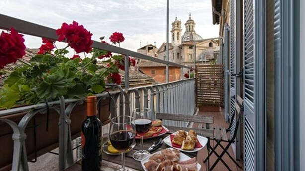 A balcony with a table set for a meal, including wine, bread, and meat. - Le Suite Del Barone (Rome)
