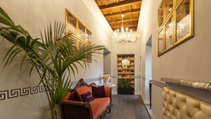 A hallway with a sofa, a potted plant, a chandelier, and a fireplace. - Le Suite Del Barone (Rome)