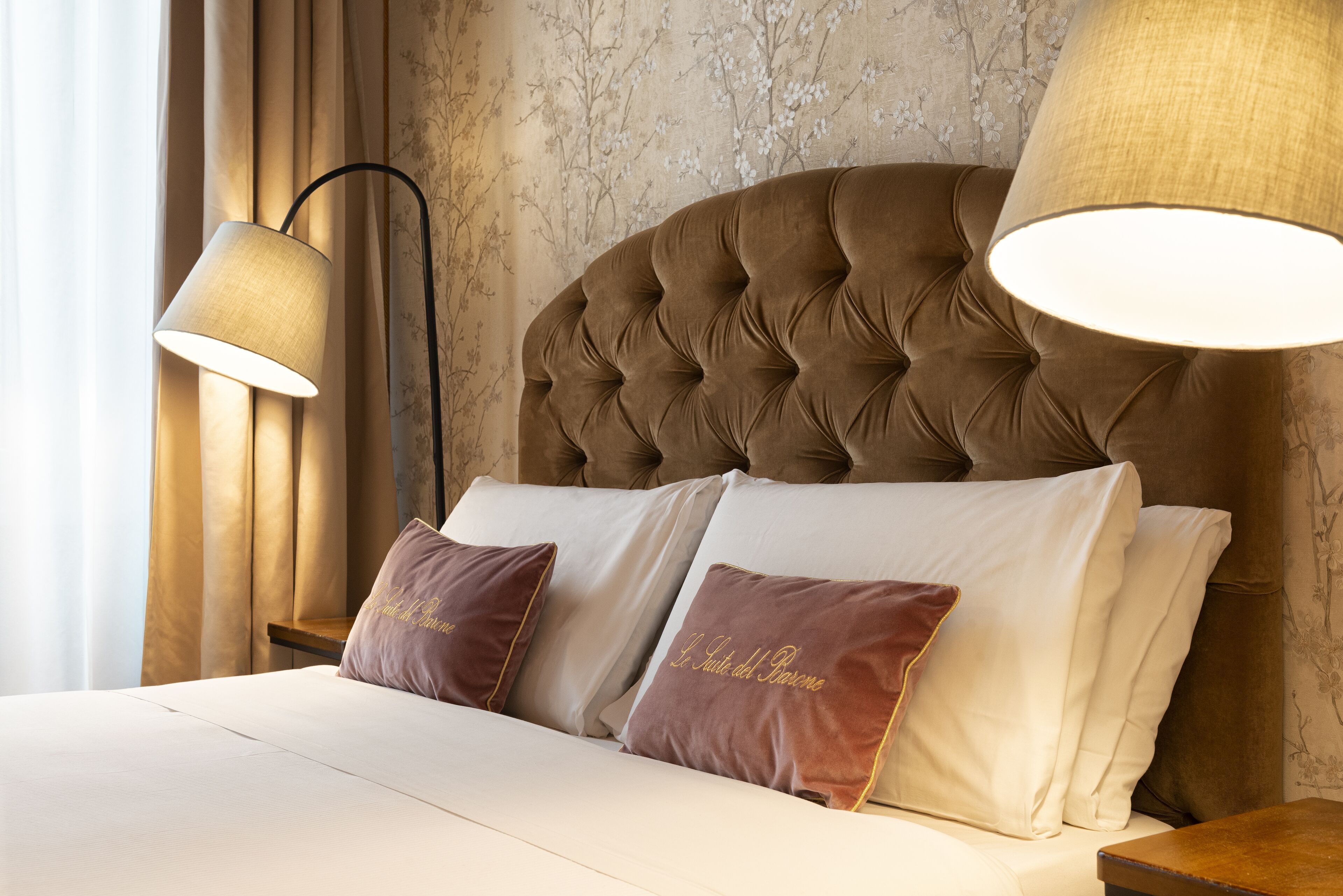 A neatly made bed with two pillows, a tufted headboard, and two wall-mounted lamps.