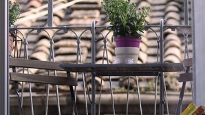A balcony with a metal railing, a potted plant, a candle, and three glasses. - Le Suite Del Barone (Rome)