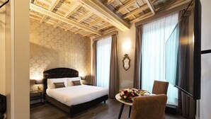 A hotel room with a large bed, a small table with flowers, a chair, and a television. - Le Suite Del Barone (Rome)