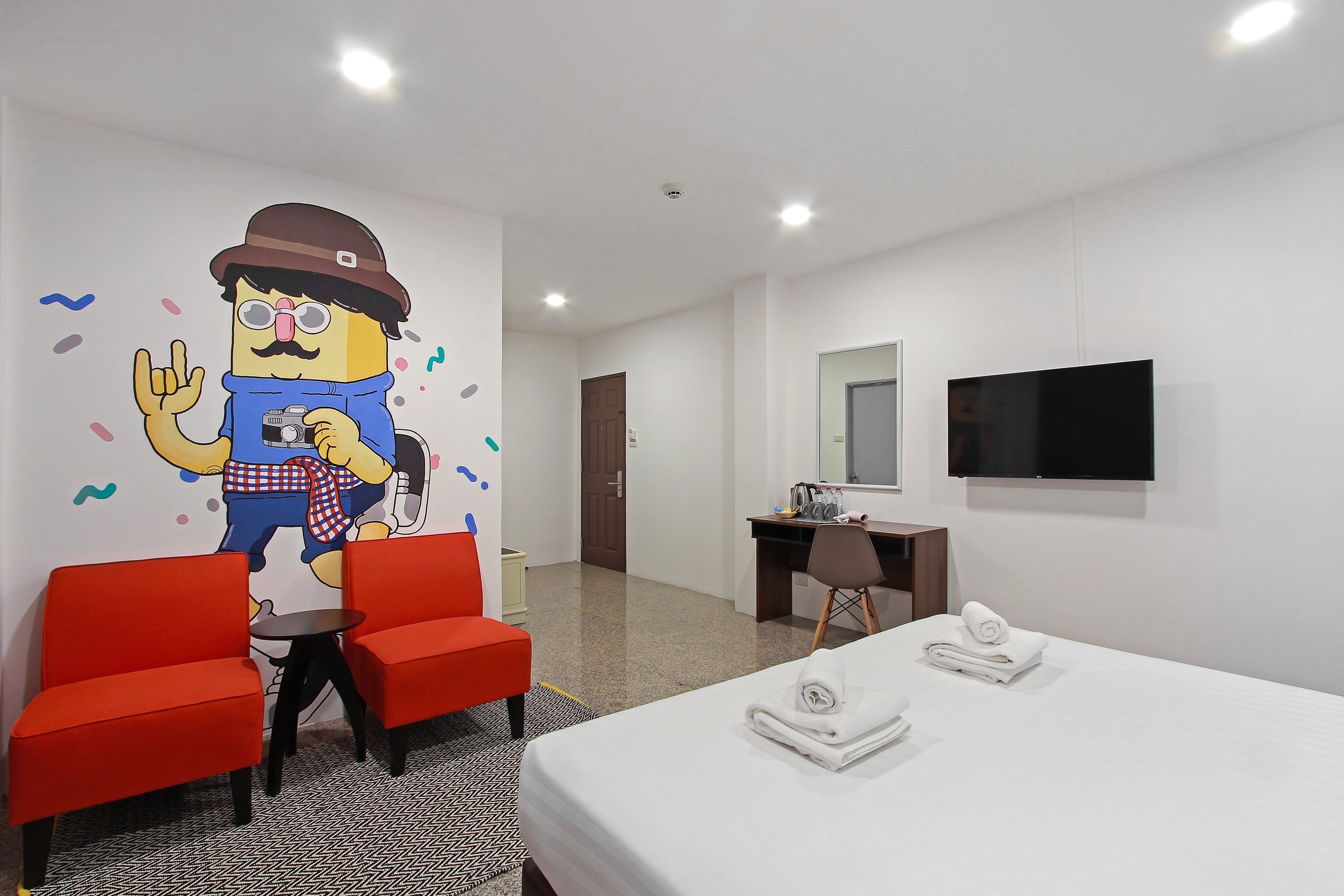 A hotel room with a bed, two red chairs, a desk, a TV, and a wall mural.