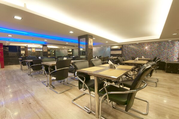 A modern restaurant with high tables and chairs, a patterned wall, and a ceiling with blue lighting.