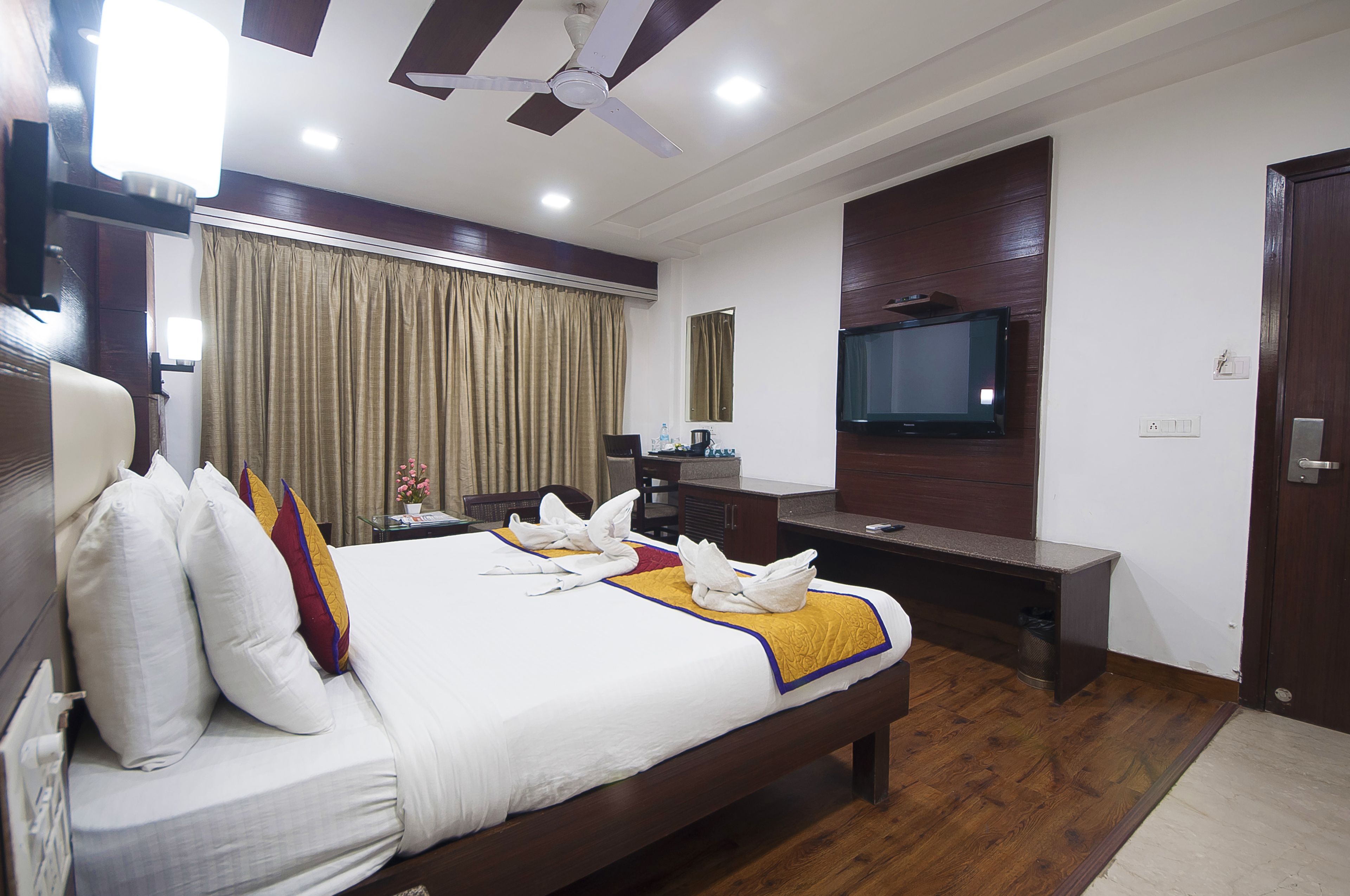 A hotel room with a bed, a desk, a television, and a ceiling fan.