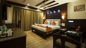 Habitación de hotel con cama, mesita de noche, escritorio, silla, cortinas y un cuadro en la pared.