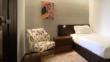 A bedroom with a bed, a nightstand, a chair, a wall-mounted air conditioner, and a rug.