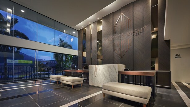A modern reception area with a marble reception desk, comfortable seating, and a large window offering a view of the outside. - Tropics Eight Suites (George Town)
