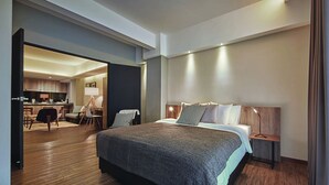 A modern hotel room with a large bed, a desk, and a dining area. - Tropics Eight Suites (George Town)