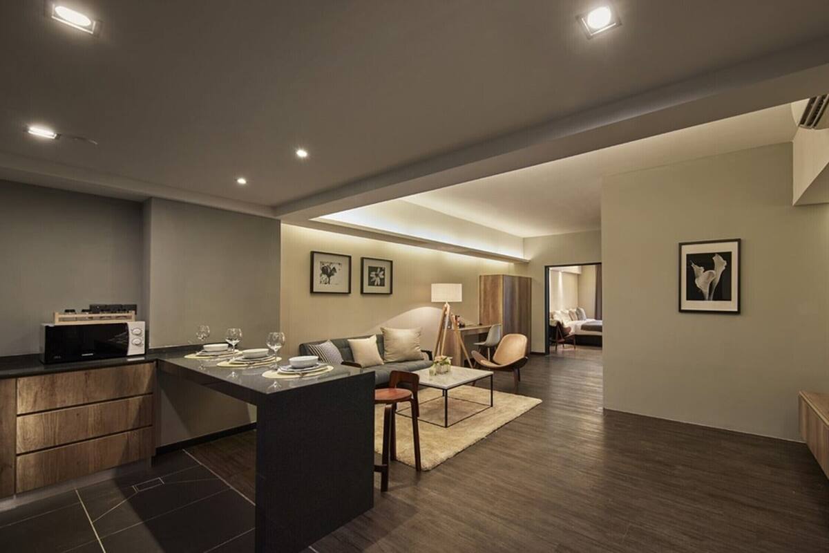 Eine moderne Küche mit Essbereich, ein Wohnzimmer mit Sofa und Sesseln sowie ein an der Wand befestigter Fernseher.