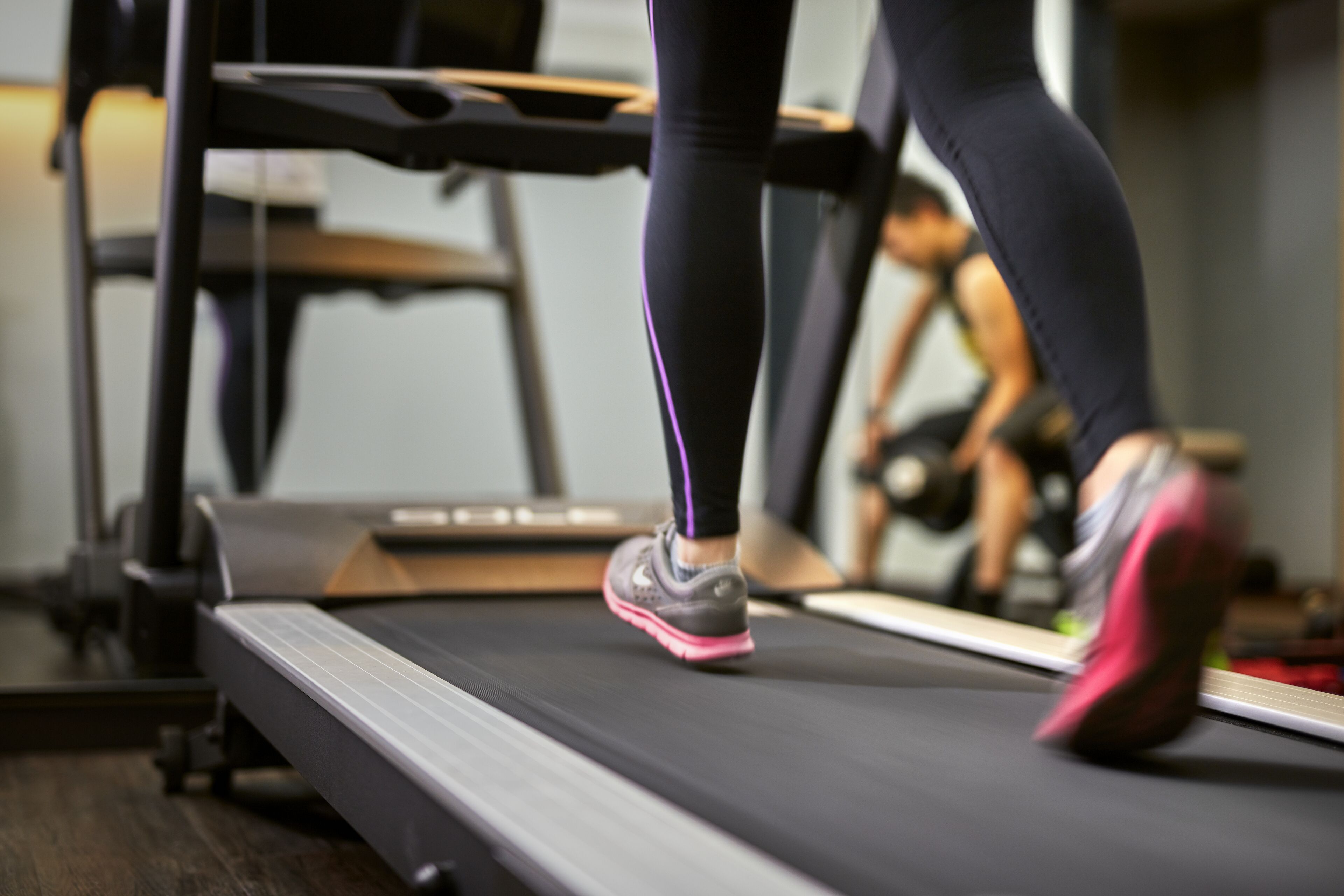 A treadmill in a gym with a mirror reflecting a person running.