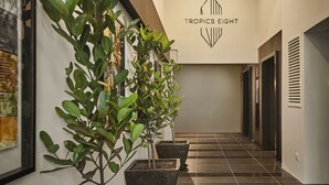 A modern hallway with potted plants, a geometric logo, and a tiled floor. - Tropics Eight Suites (George Town)