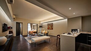 A modern hotel room with a large bed, a sitting area with a sofa and armchairs, a dining area with a table and chairs, and a kitchen with a microwave and toaster. - Tropics Eight Suites (George Town)