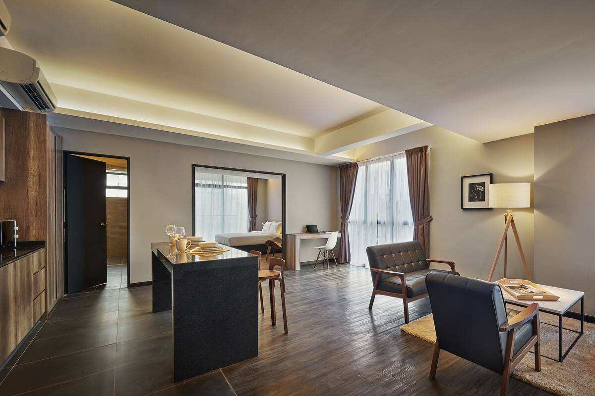 Ein modernes Hotelzimmer mit Küchenzeile, einem Esstisch mit Stühlen, einer Couch und einem Schreibtisch.