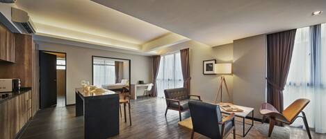 A modern hotel room with a kitchen area, a dining table with chairs, a sofa, and a desk.
