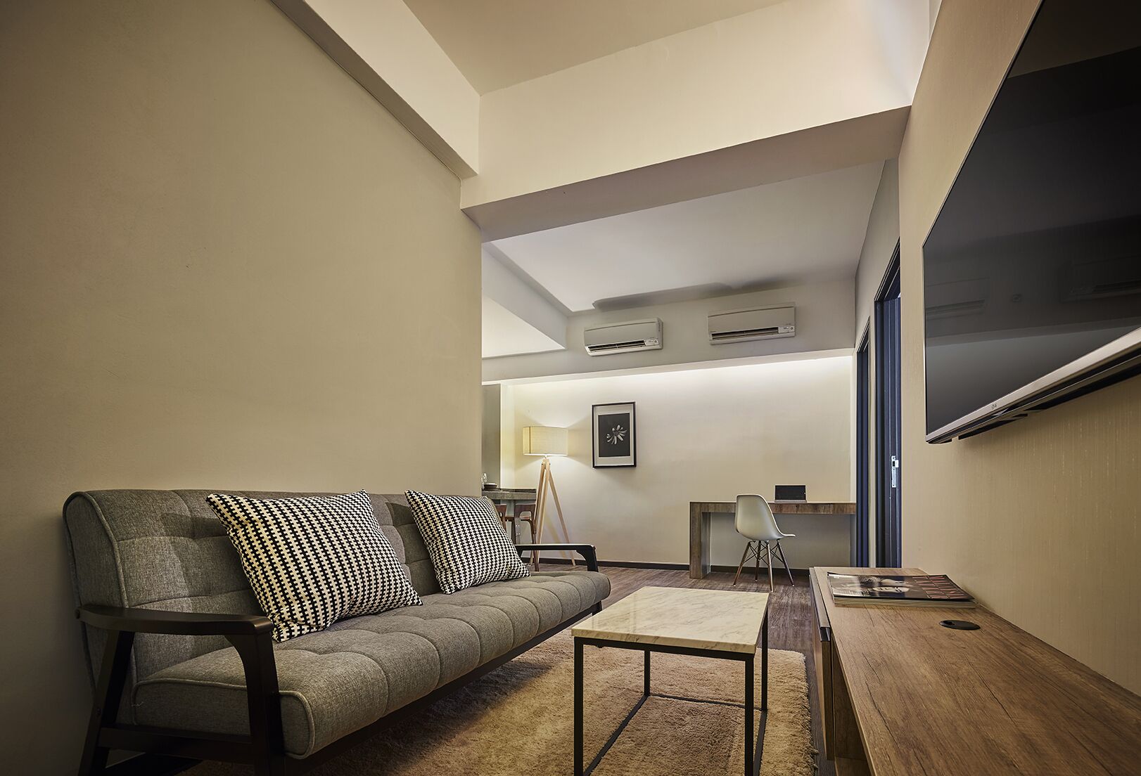 Een moderne woonkamer met een grijze bank, zwart-wit gestreepte kussens, een houten salontafel en een aan de muur bevestigde televisie.