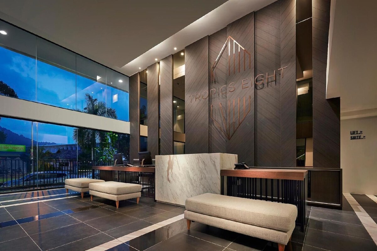 A modern hotel lobby with a reception desk, seating area, and large windows offering a view of the outdoors.