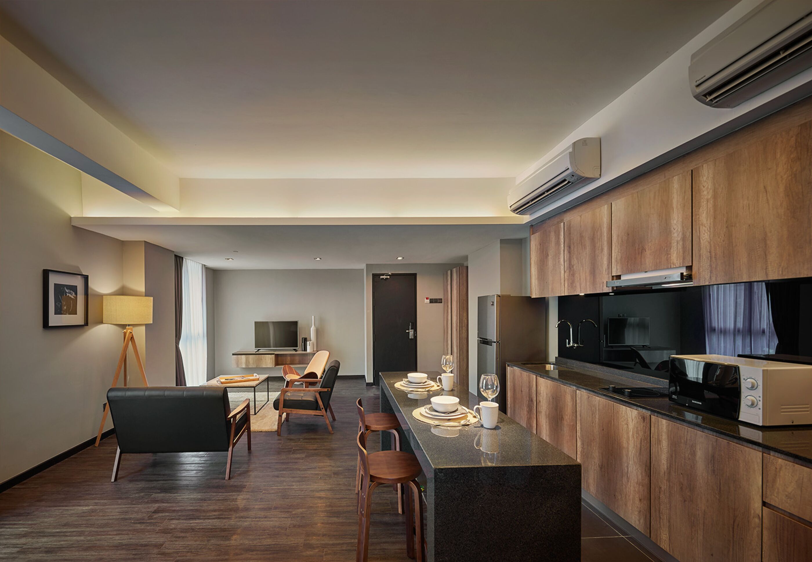 Een moderne keuken met houten kastjes, een centraal eiland met barkrukken, een eethoek met tafel en stoelen, en een televisie op de achtergrond.