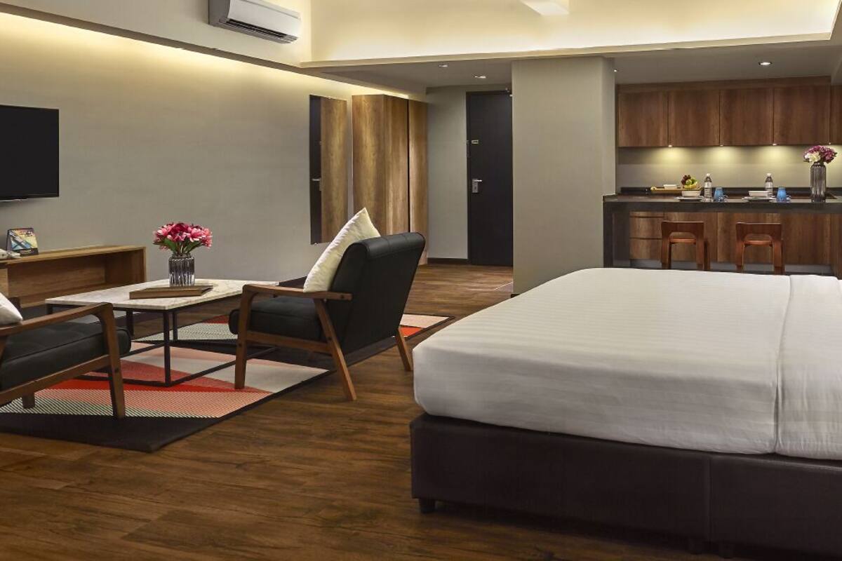 Ein modernes Hotelzimmer mit einem großen Bett, einem Schreibtisch mit Stuhl, einem Fernseher und einer Küchenzeile.
