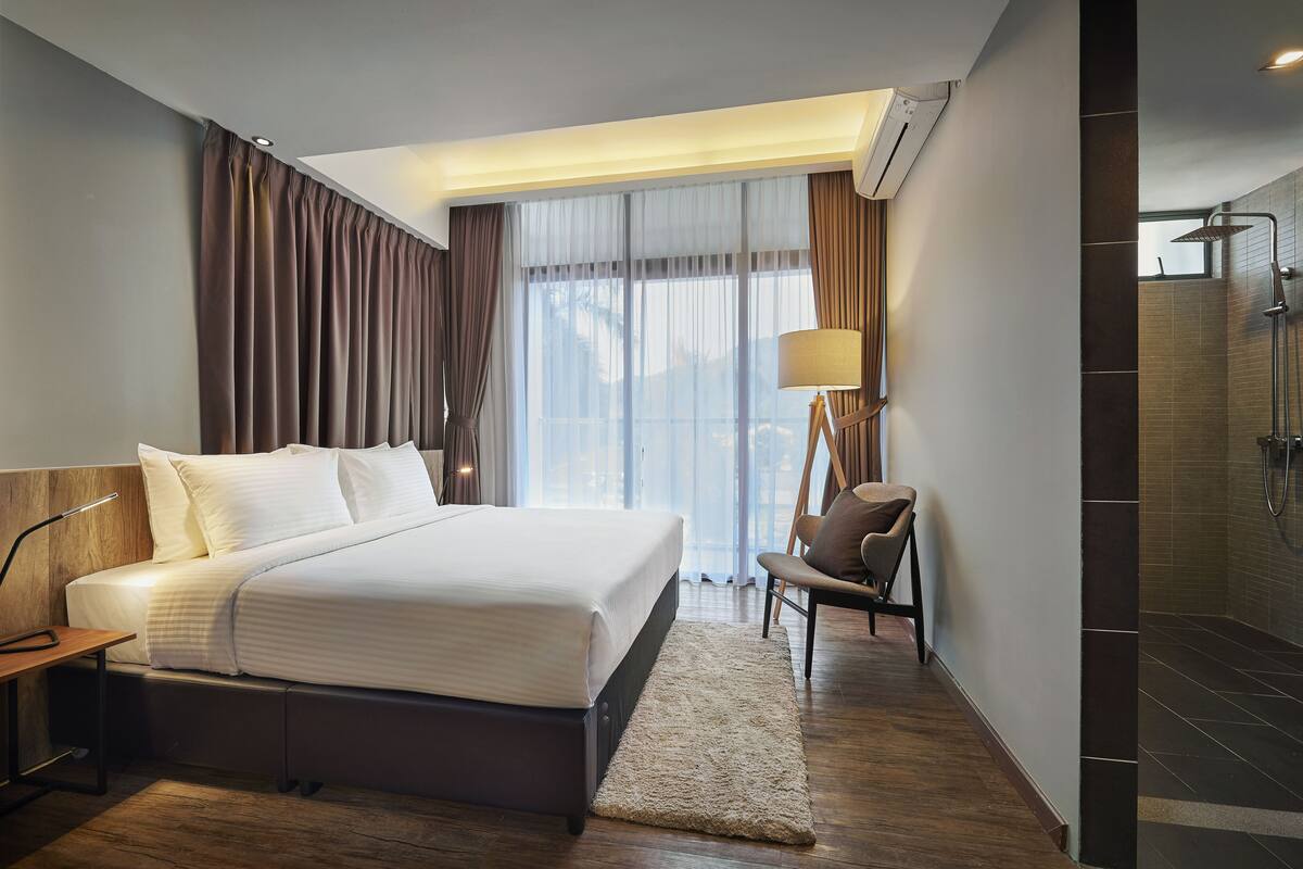Ein modernes Hotelzimmer mit einem großen Bett, einem Schreibtisch, einem Stuhl, einer Stehlampe und einer Duschkabine.