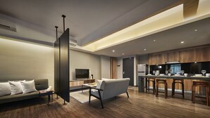 A modern living room with a sofa, a coffee table, and a TV. There is a kitchen area with wooden cabinets and a refrigerator. - Tropics Eight Suites (George Town)