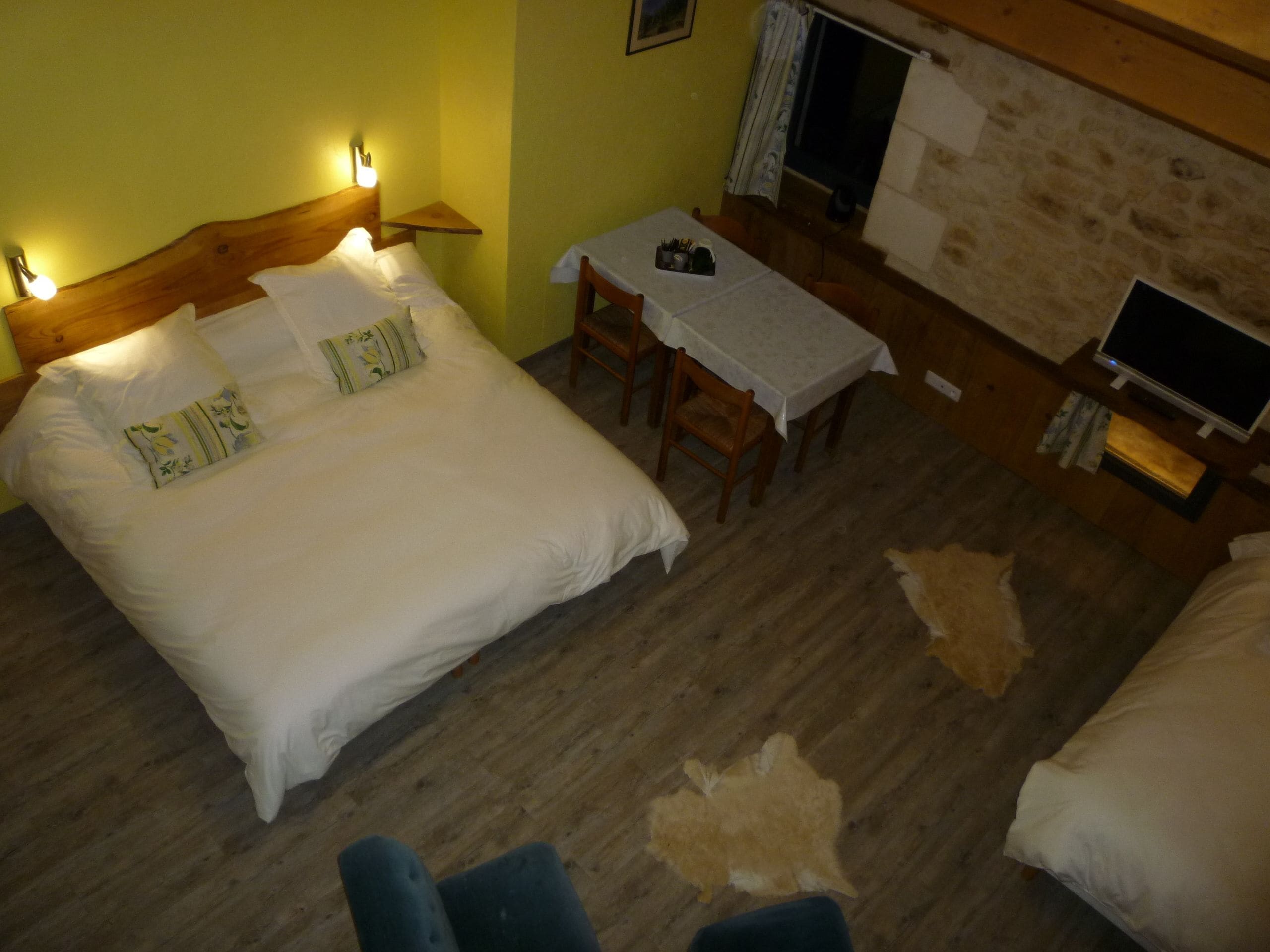 A room with a bed, a small table with a chair, a television, and a fireplace.