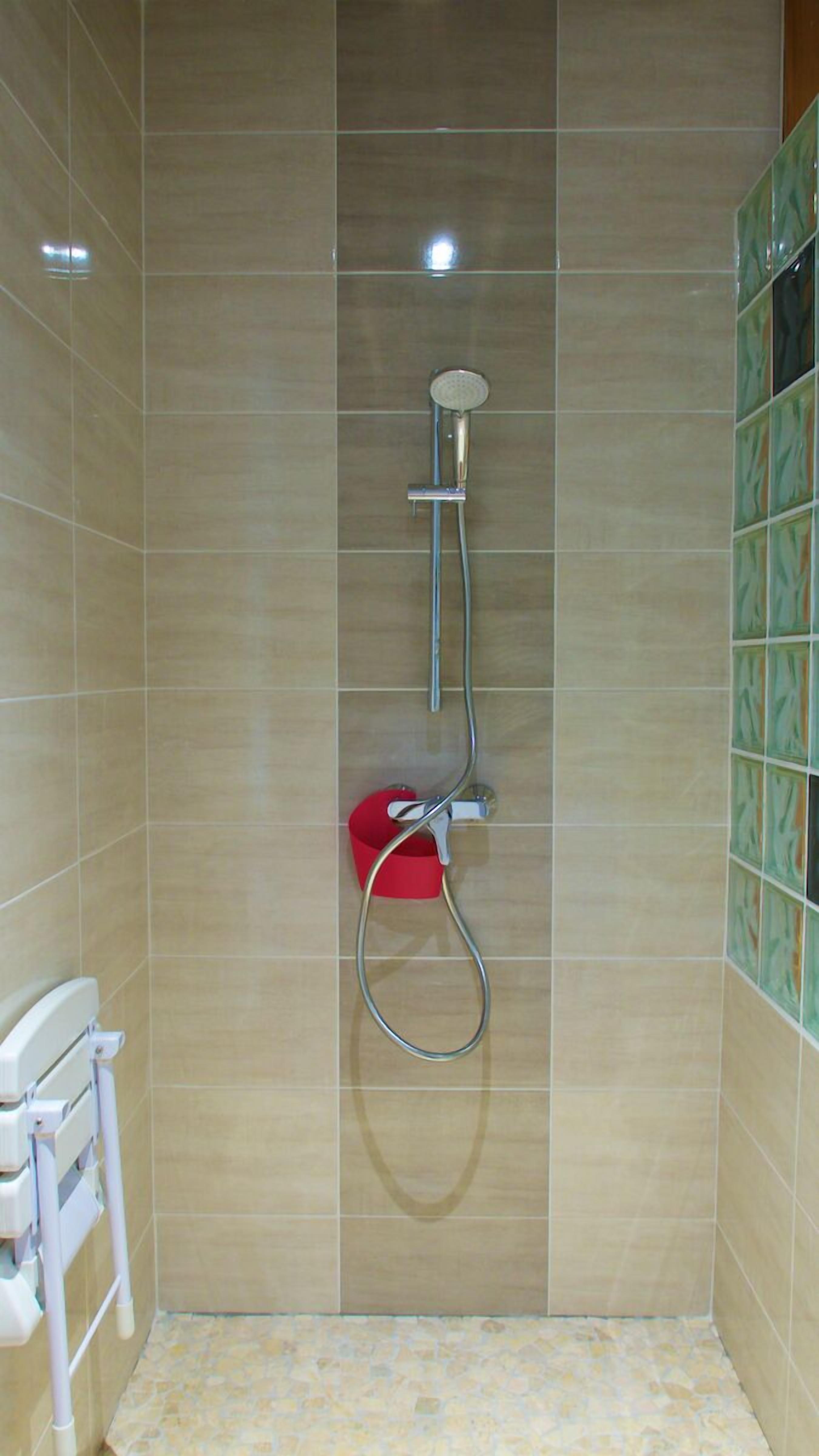 Un espace douche avec des carreaux de couleur beige, une douchette et un seau rouge.