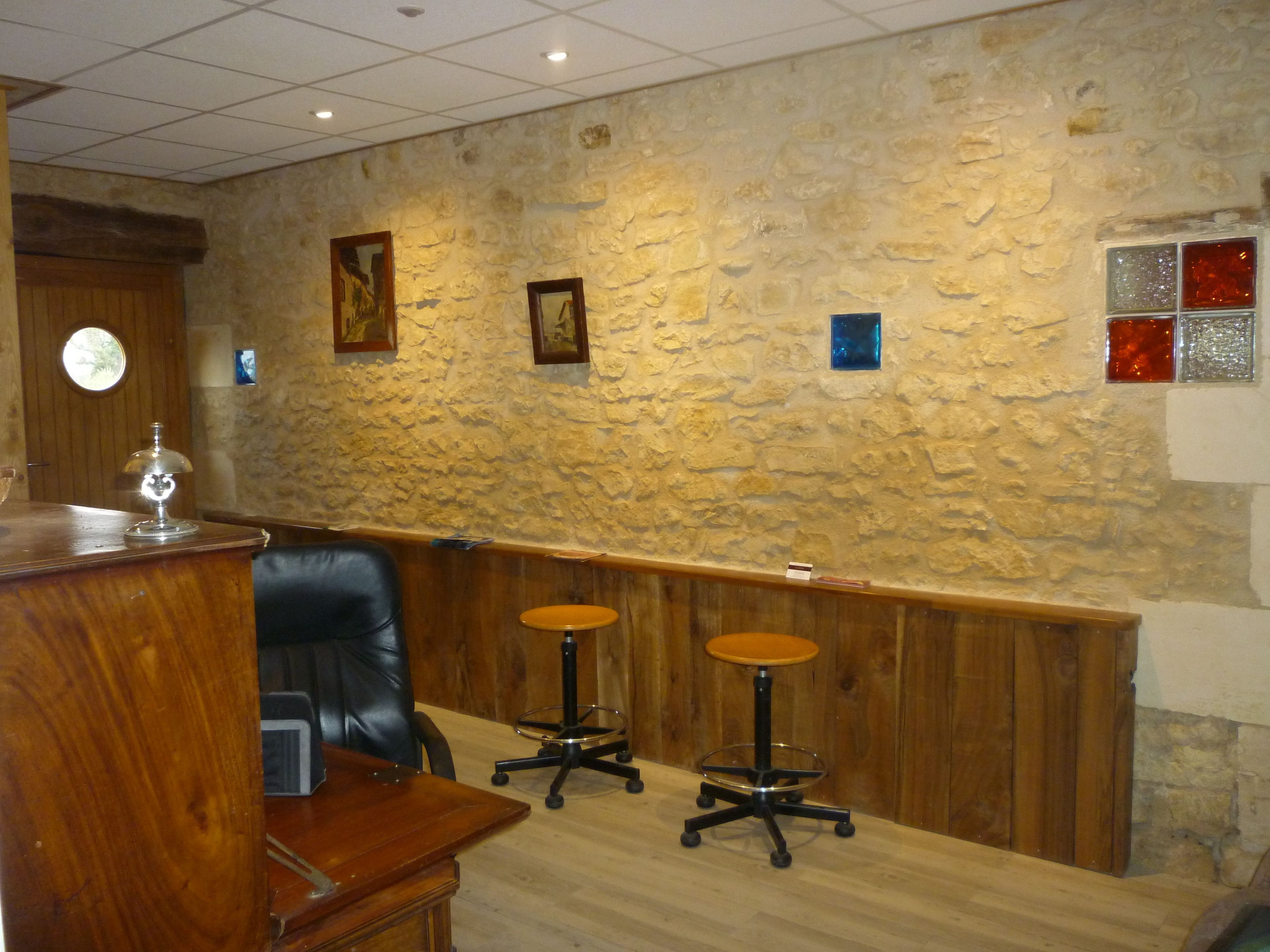 Uma área de recepção com uma mesa de madeira, uma cadeira de couro preto e dois banquinhos.