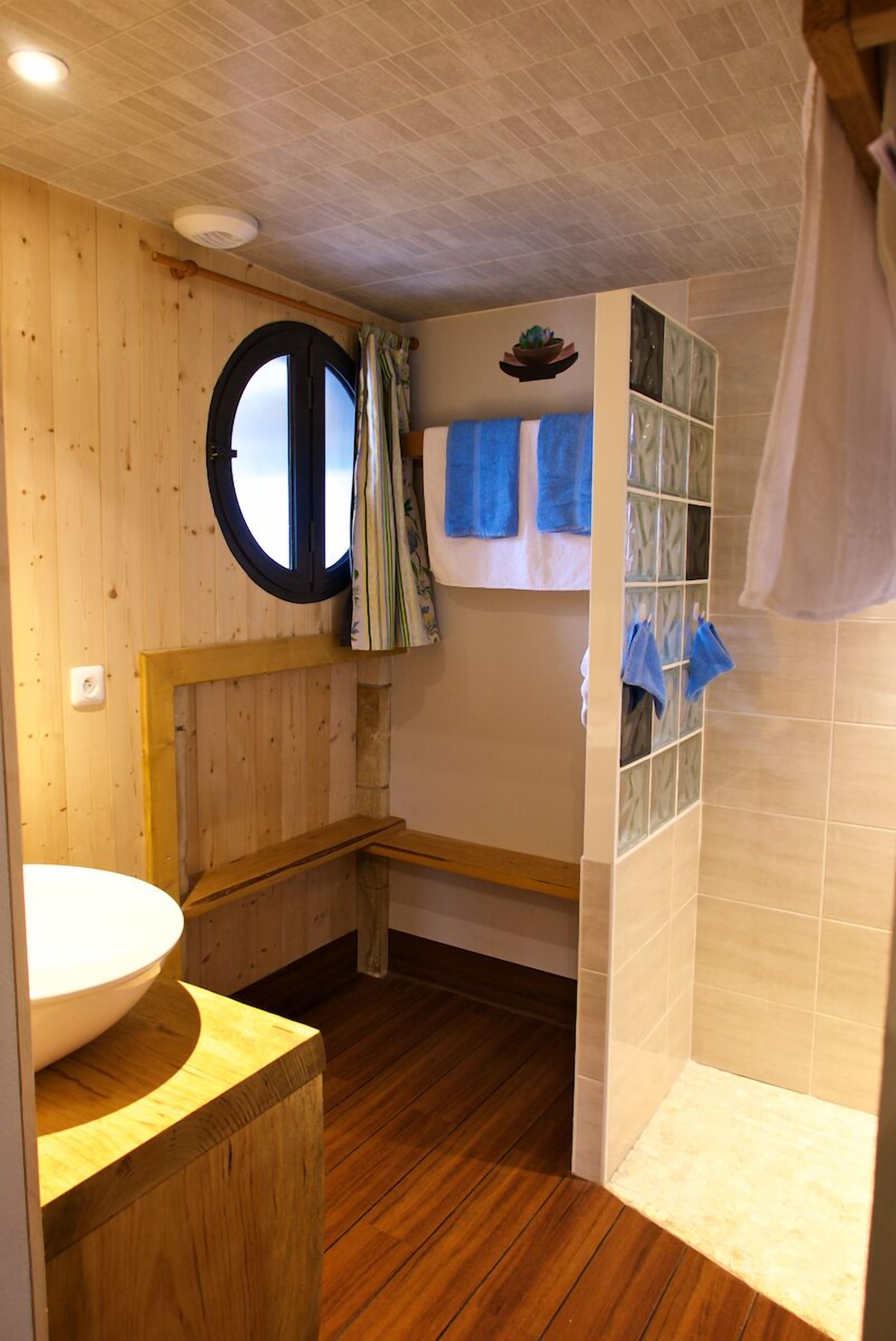 A bathroom with wooden walls, a round window, a sink, and a shower area.