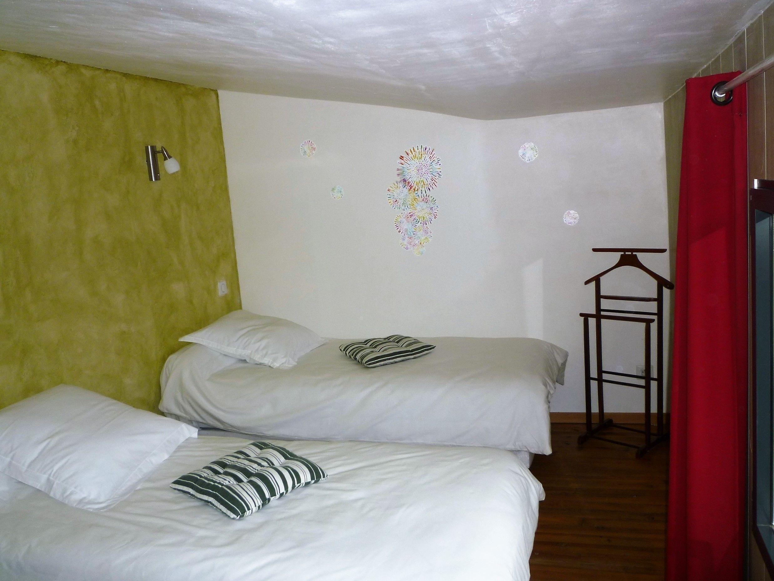 Une chambre avec deux lits, un rideau rouge et une horloge murale.