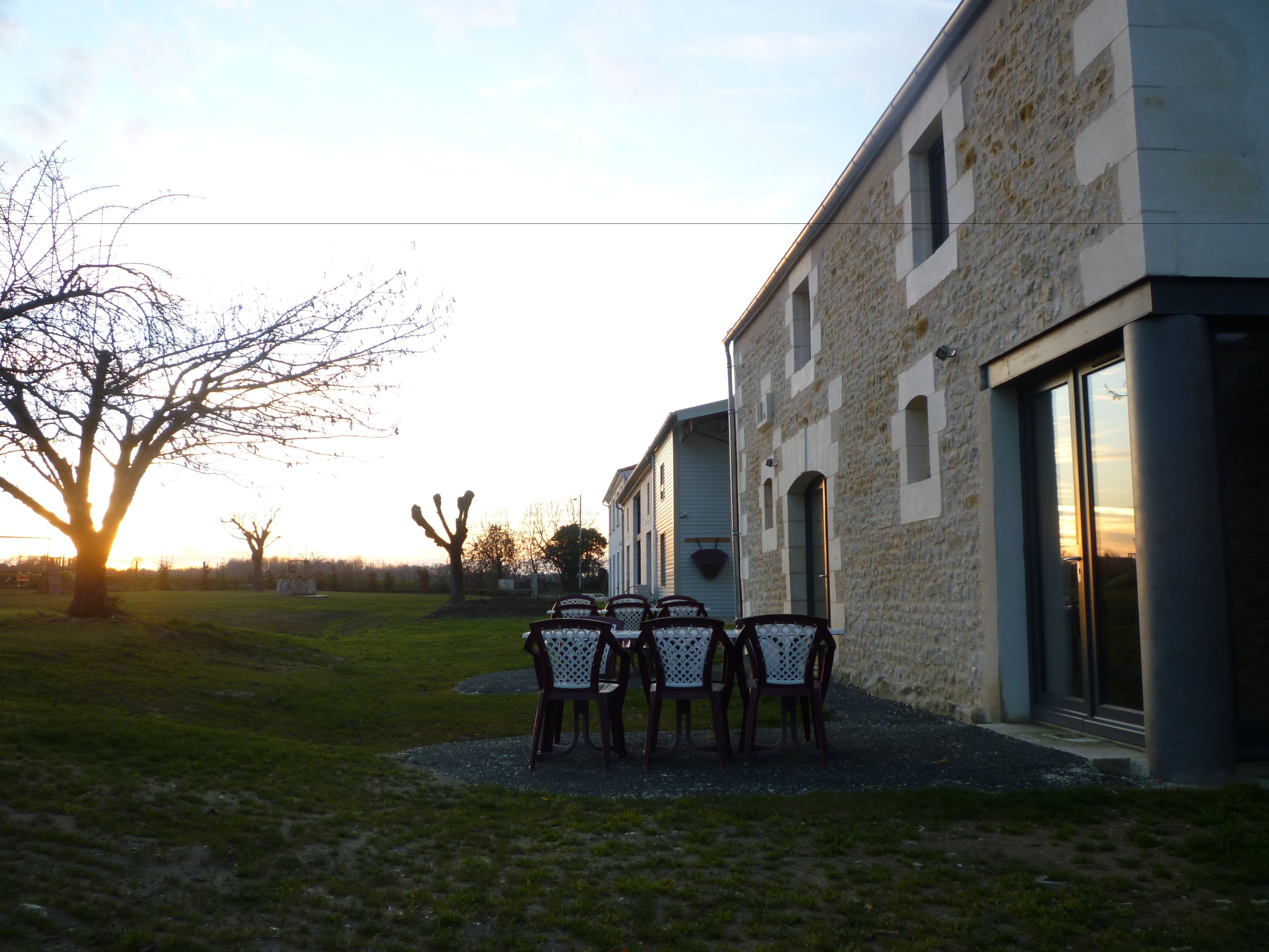 Un bâtiment à la façade en pierre, un patio avec des chaises et un arbre au premier plan.