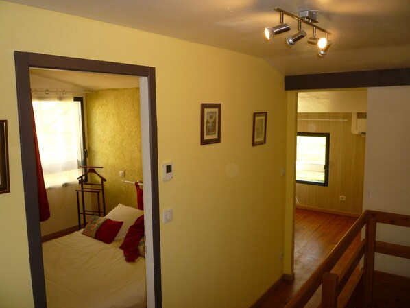 A bedroom with a bed, a mirror, a window with curtains, a wooden floor, and a ceiling light fixture.