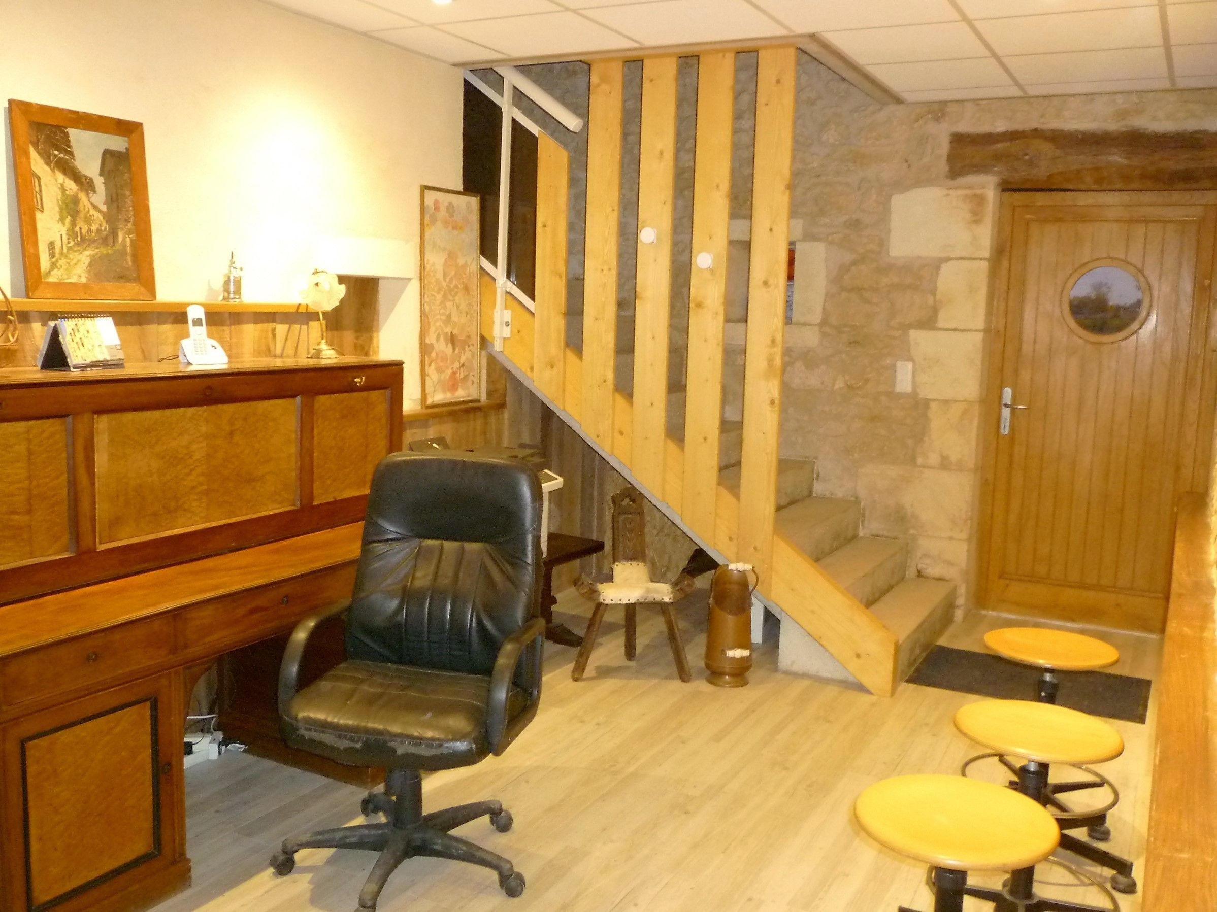 A reception area with a wooden desk, a black office chair, a staircase with wooden railings, and a stone wall.