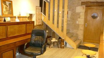 A reception area with a wooden desk, a black office chair, a staircase with wooden railings, and a stone wall.