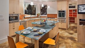 Une cuisine moderne avec des meubles en bois, des appareils en acier inoxydable et un îlot central agrémenté de chaises orange.